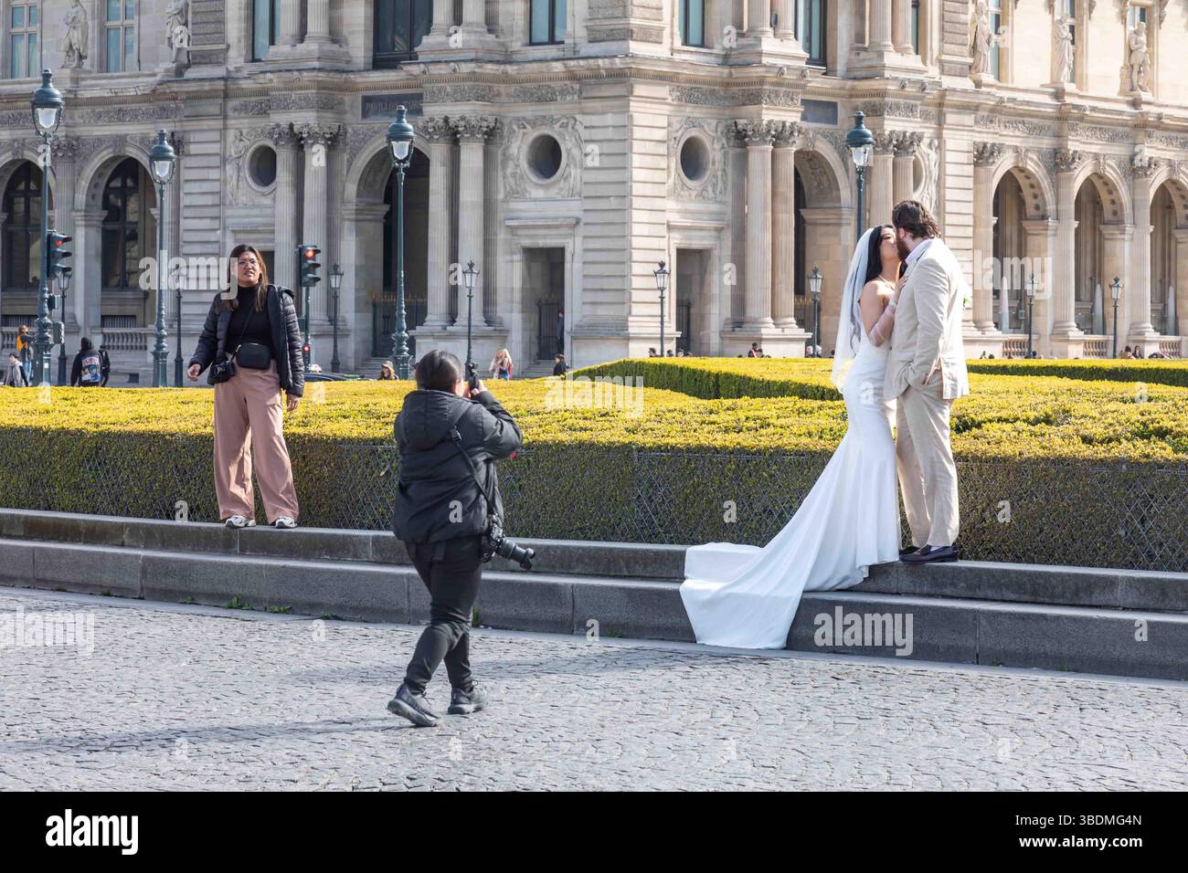 Mariés et mariés s'embrassant et posant pour un photographe de mariage devant le Palais du Louvre à Paris, France Banque D'Images
