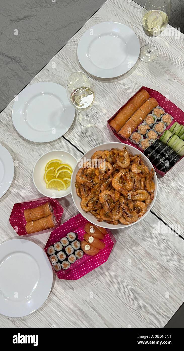 Style de vie. Sur la table se trouve une assiette de crevettes et de sushis, des assiettes et des verres de vin. Rencontre d'amis. - Image de stock capturée avec un smartphone