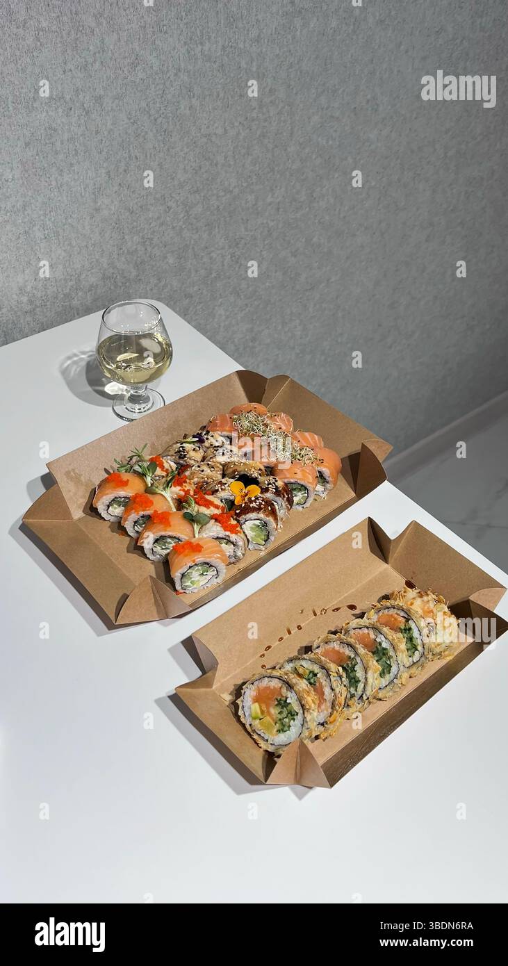 Un verre de vin sur une table blanche. Sushi, rouleaux, dans des boîtes en carton. - Image de stock capturée avec un smartphone