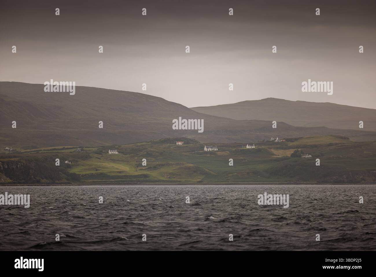 Les chalets blancs parsèment le paysage côtier vert sous un ciel gris doux sur l'île de Skye, en Écosse, avec de douces collines en arrière-plan. Banque D'Images Les chalets blancs parsèment le paysage côtier vert sous un ciel gris doux sur l'île de Skye, en Écosse, avec de douces collines en arrière-plan. Banque D'Images