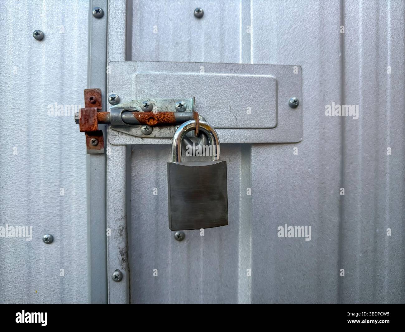 Photographie d'un vieux cadenas qui sécurise un système de verrouillage rouillé de porte à cadenas à un œil sur un ancien hangar galvanisé dans un jardin résidentiel. Banque D'Images