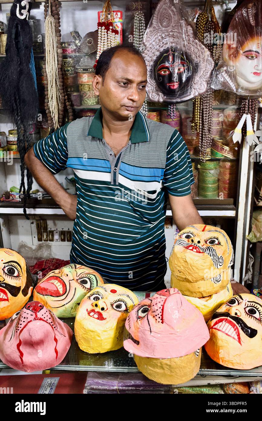 Un vendeur de masques se tient derrière des masques rituels hindous en papier peint mâché dans un magasin au bazar Shankhari (rue hindoue), Old Dhaka, Bangladesh. Banque D'Images