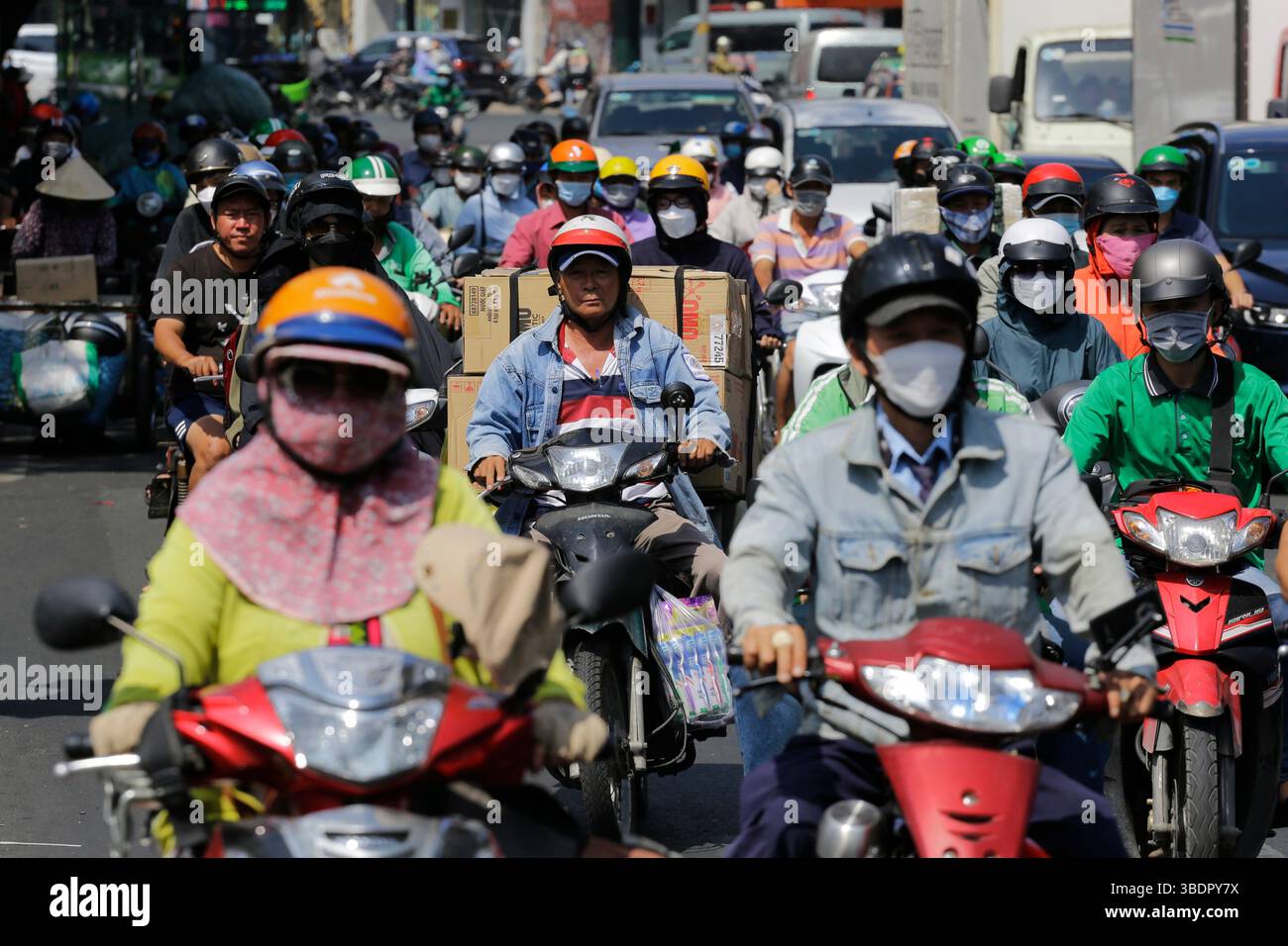Ho Chi Minh, Vietnam - 23 décembre 2022 : des motocyclistes, dont certains portent un masque facial, traversent une avenue animée à Saigon. Banque D'Images