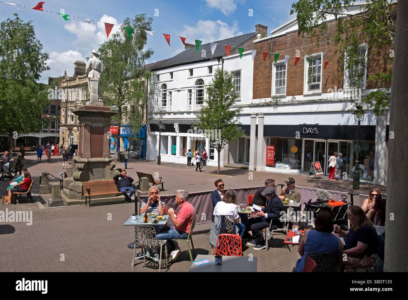 Les gens assis à des tables et des chaises mangeant devant le restaurant Cofio Lounge au printemps 2025 Sunshine Guildhall Square Carmarthen Wales UK KATHY DEWITT Banque D'Images