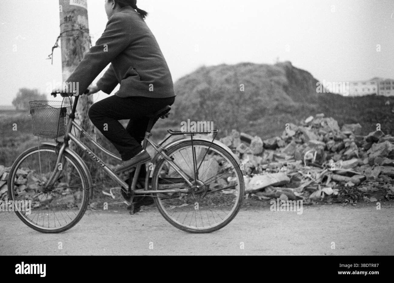 Femme cyclant devant les décombres en Chine rurale, début des années 2010 Banque D'Images