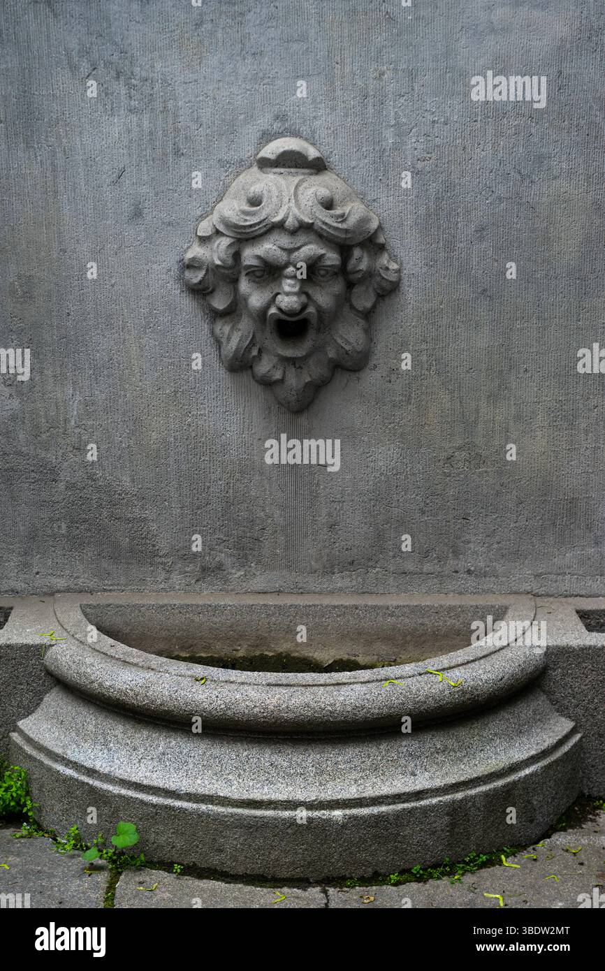 Vieille fontaine noire avec de l'eau potable sur le mur de la vieille maison. Banque D'Images