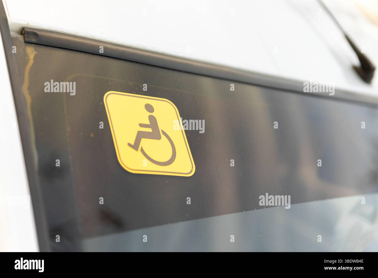Gros plan d'un autocollant jaune d'accessibilité pour fauteuil roulant sur la vitre d'un véhicule, indiquant l'accès aux transports pour les personnes handicapées. Banque D'Images