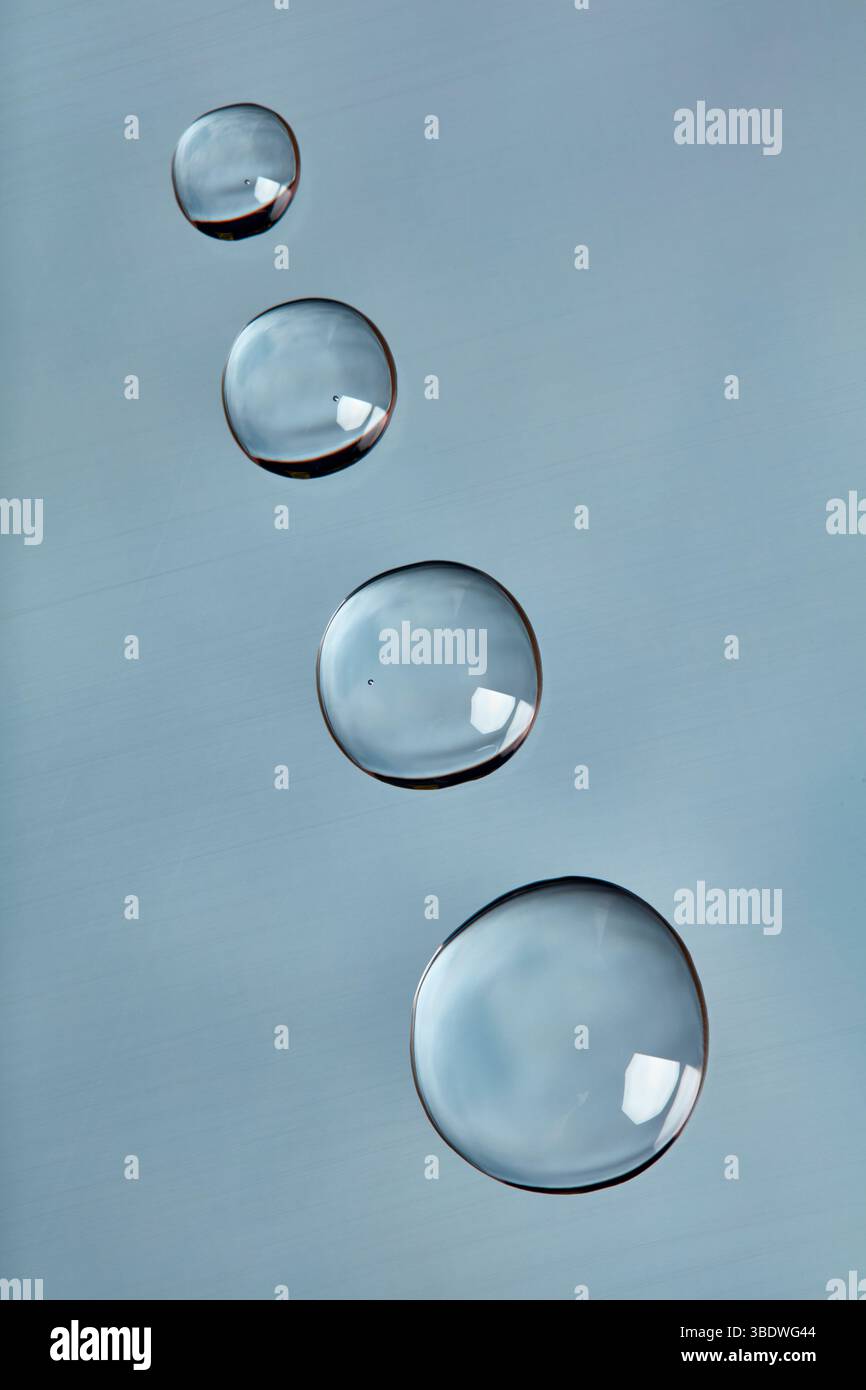 Gouttelettes d'eau disposées en diagonale sur une surface lisse bleu clair. Banque D'Images