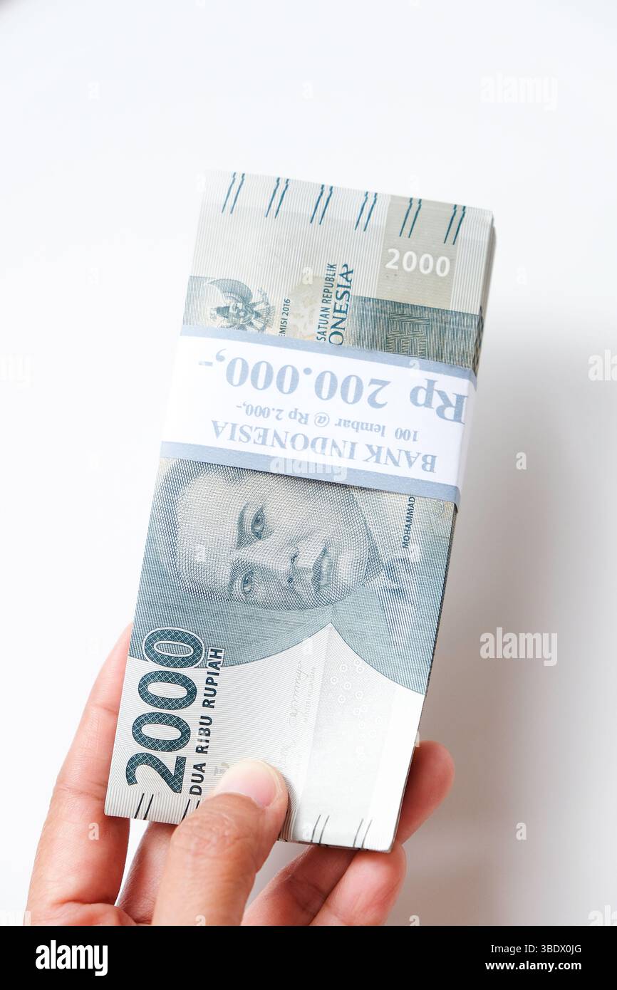 Pekanbaru, Indonésie - 21 mars 2025 : main tenant des billets de banque rupiah indonésiens RP 2,000 isolés sur fond blanc pour THR sur Eid al-Fitr ou Lebara Banque D'Images