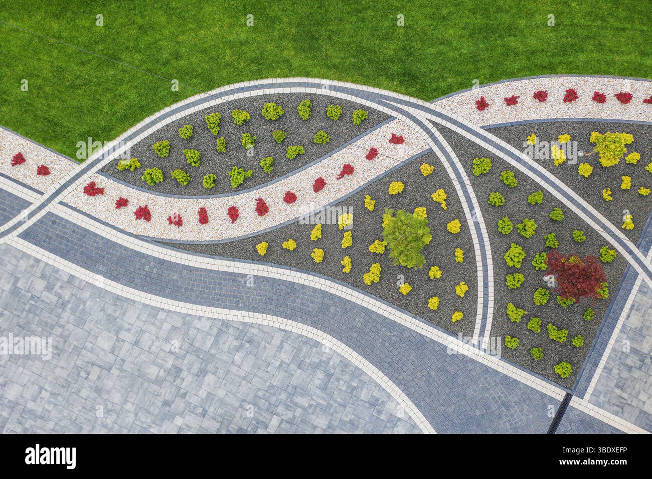 Les parterres de fleurs vibrantes couronnent gracieusement au milieu d'un paysage bien entretenu, avec des pierres soigneusement disposées formant des chemins artistiques dans un parc public. Banque D'Images