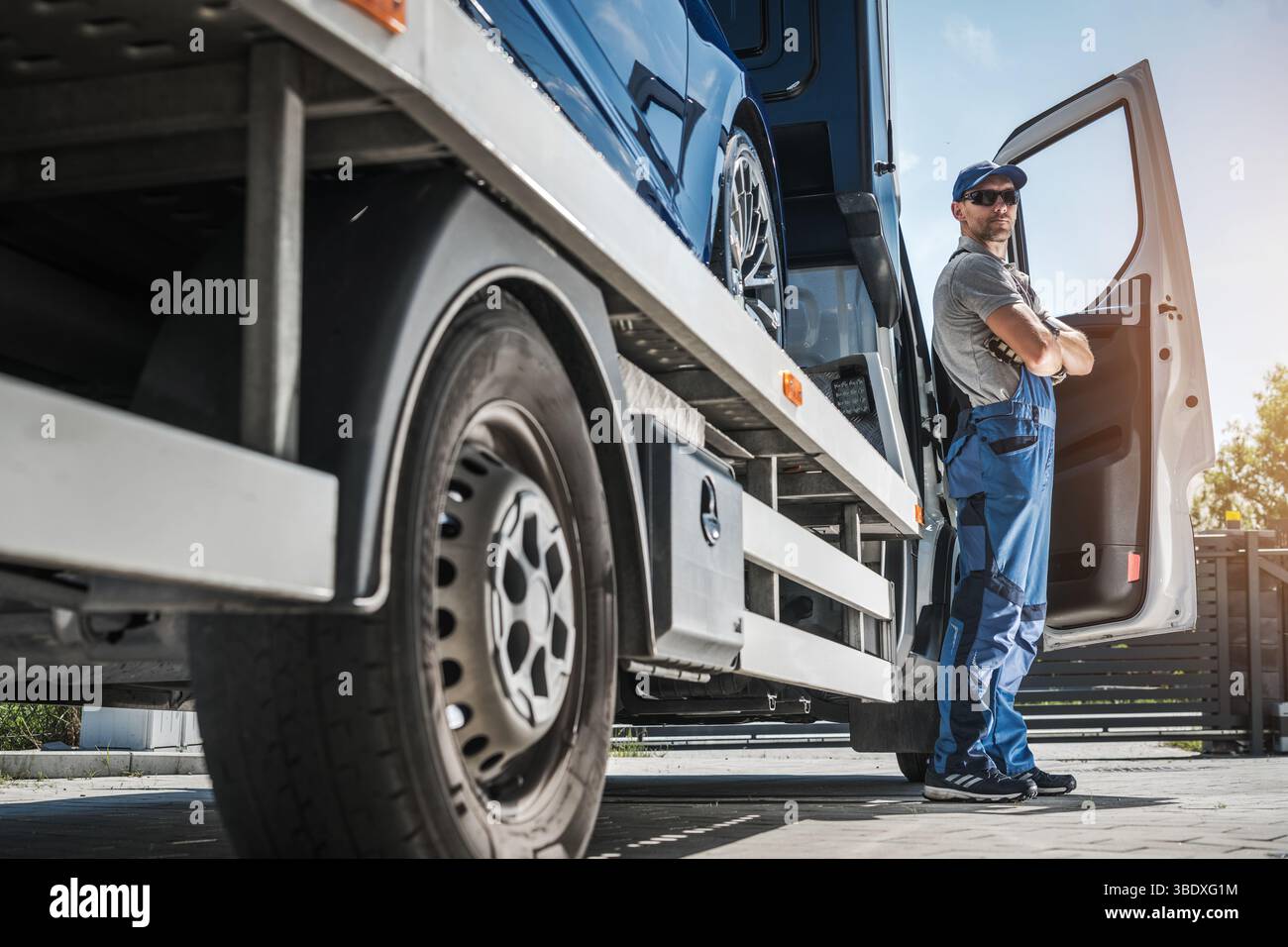 Un travailleur du transport se tient près d’une porte de camion ouverte, prêt à charger un véhicule sur la remorque d’un site logistique pendant la journée. Banque D'Images