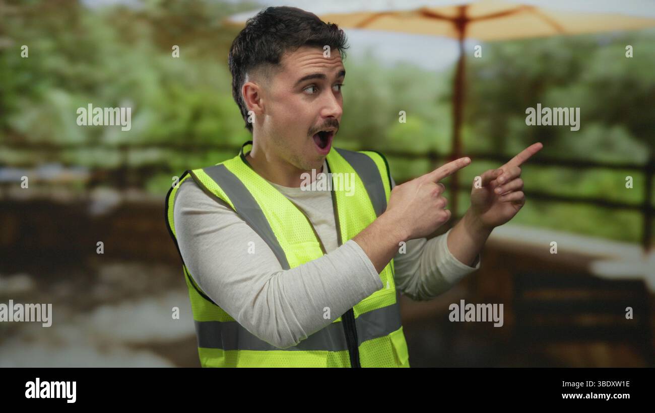 Jeune homme en pointes de gilet réfléchissant surpris dans un cadre de parc avec une verdure luxuriante sous un grand parapluie, évoquant la curiosité dans un environnement extérieur Banque D'Images