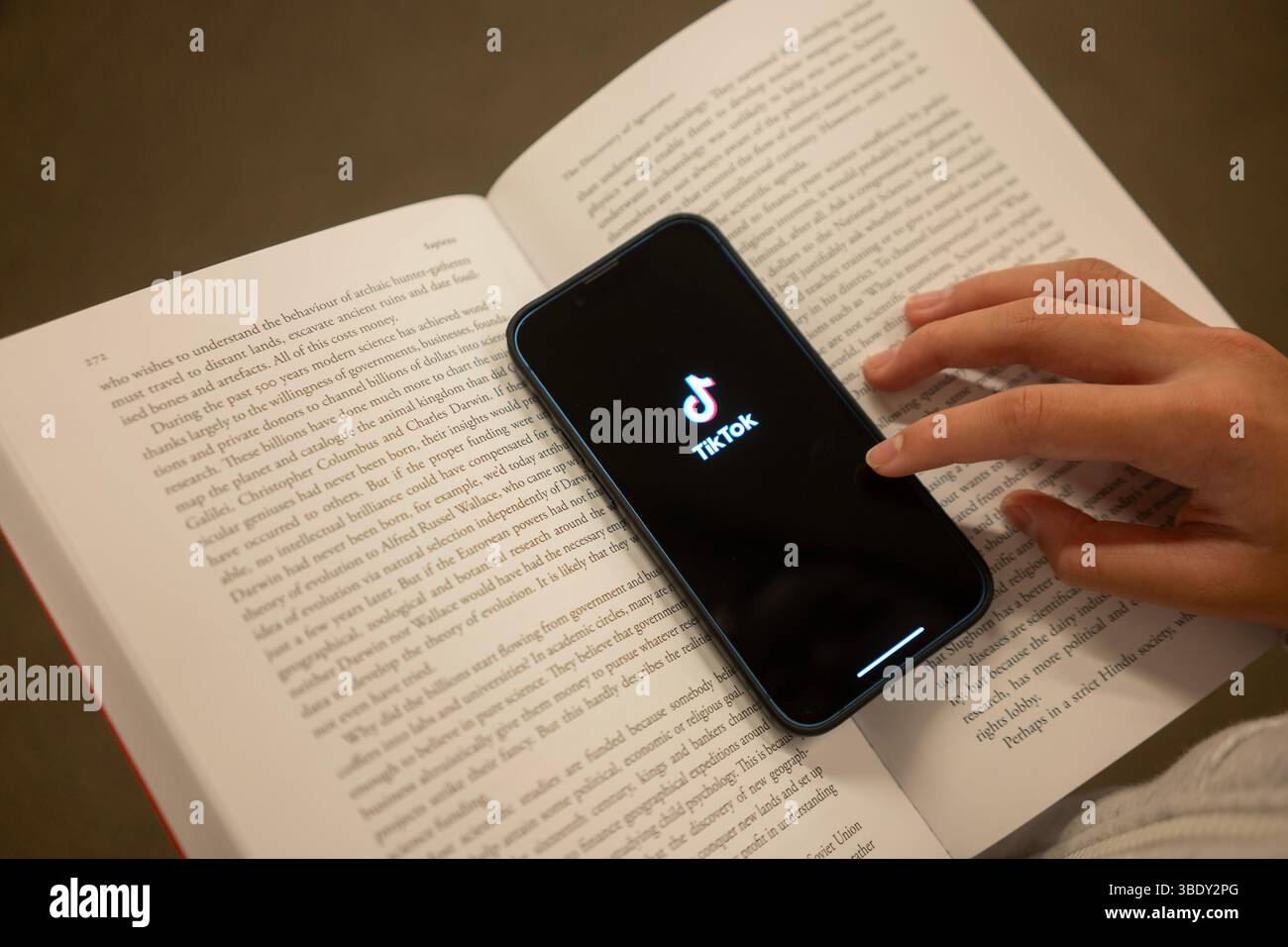 Un adolescent ouvre l'application TikTok à partir d'un iPhone en lisant « Sapiens », un livre de non-fiction de Yuval Noah Harari et une mission d'études sociales. Banque D'Images