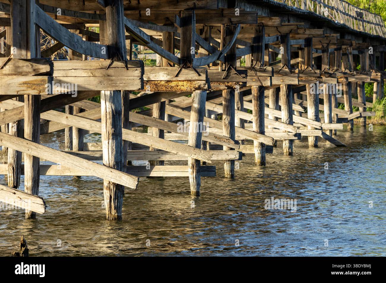 Un charmant pont piétonnier en bois s'étend sur la rivière, ses planches altérées offrant un chemin rustique à travers la nature. Le flux serein du ri Banque D'Images