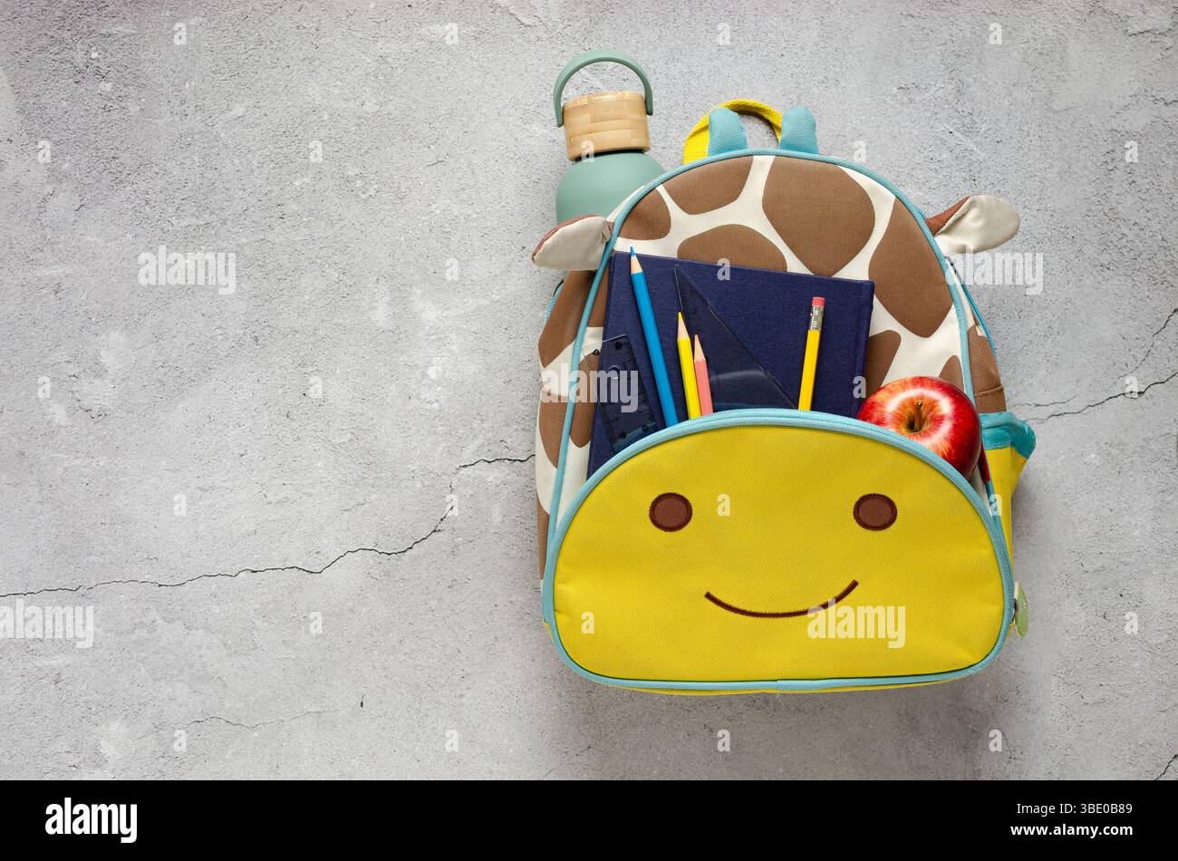 Sac à dos sur le thème de la girafe rempli de fournitures scolaires, une bouteille d'eau et une pomme prête pour l'école. Concept de retour à l'école. Banque D'Images