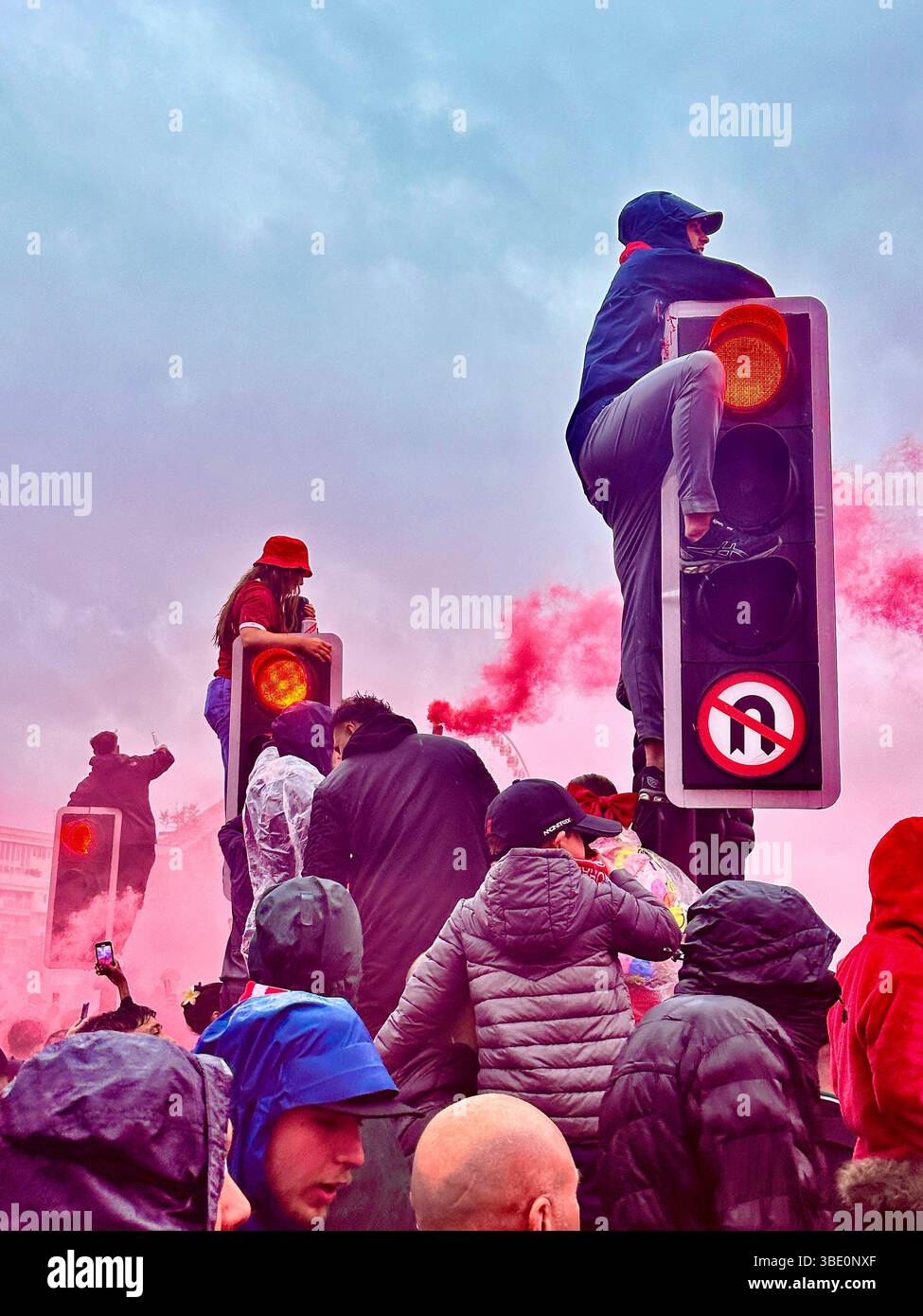 Les fans escaladent les feux de circulation dans un environnement de fumée rouge, Strand Street, Liverpool, Royaume-Uni, a hâte de voir le Liverpool FC Parade avec le trophée de la premier League. Mai 26 2025 - Image de stock capturée avec un smartphone