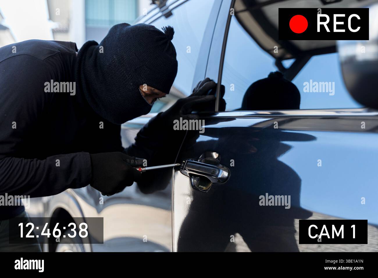 Voleur masqué pris sur la caméra de surveillance à l'aide d'un tournevis pour pénétrer dans une voiture garée. Concept de crime, vol de voiture, vidéo CCTV, sécurité awaren Banque D'Images