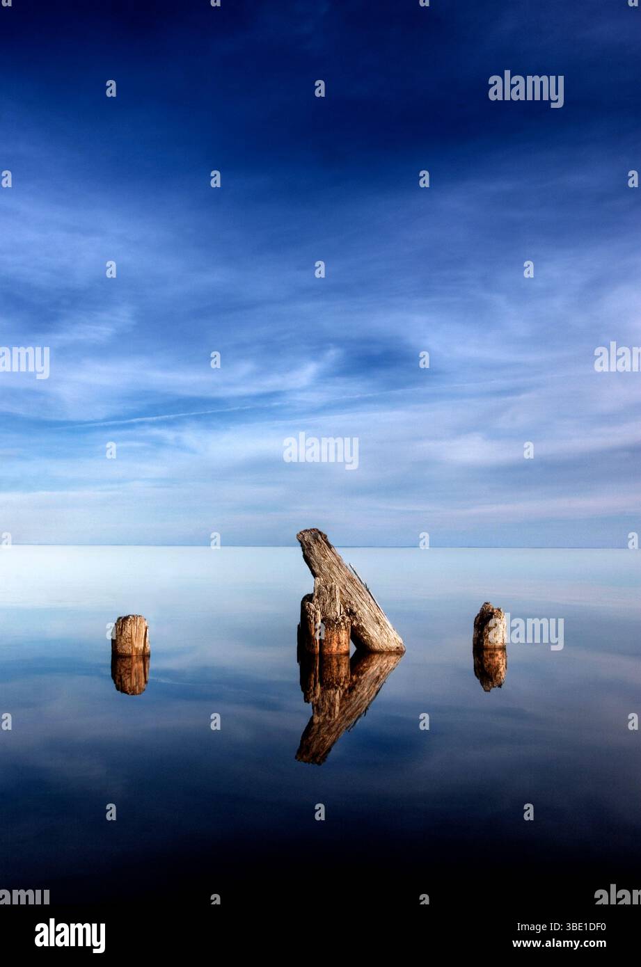 Les poteaux en bois altérés se reflètent dans un lac calme et vitreux Banque D'Images
