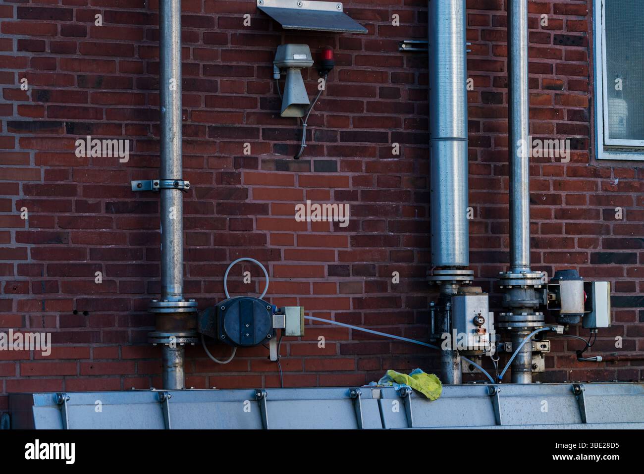 Des tuyaux métalliques et divers équipements sont installés sur un mur de briques rouges. Le cadre semble industriel, sans activité humaine visible. La configuration Banque D'Images