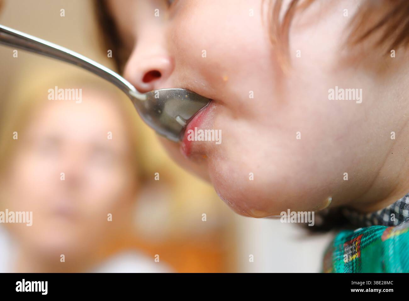 Un gamin mangeant de la soupe avec l'aide de sa mère. Banque D'Images