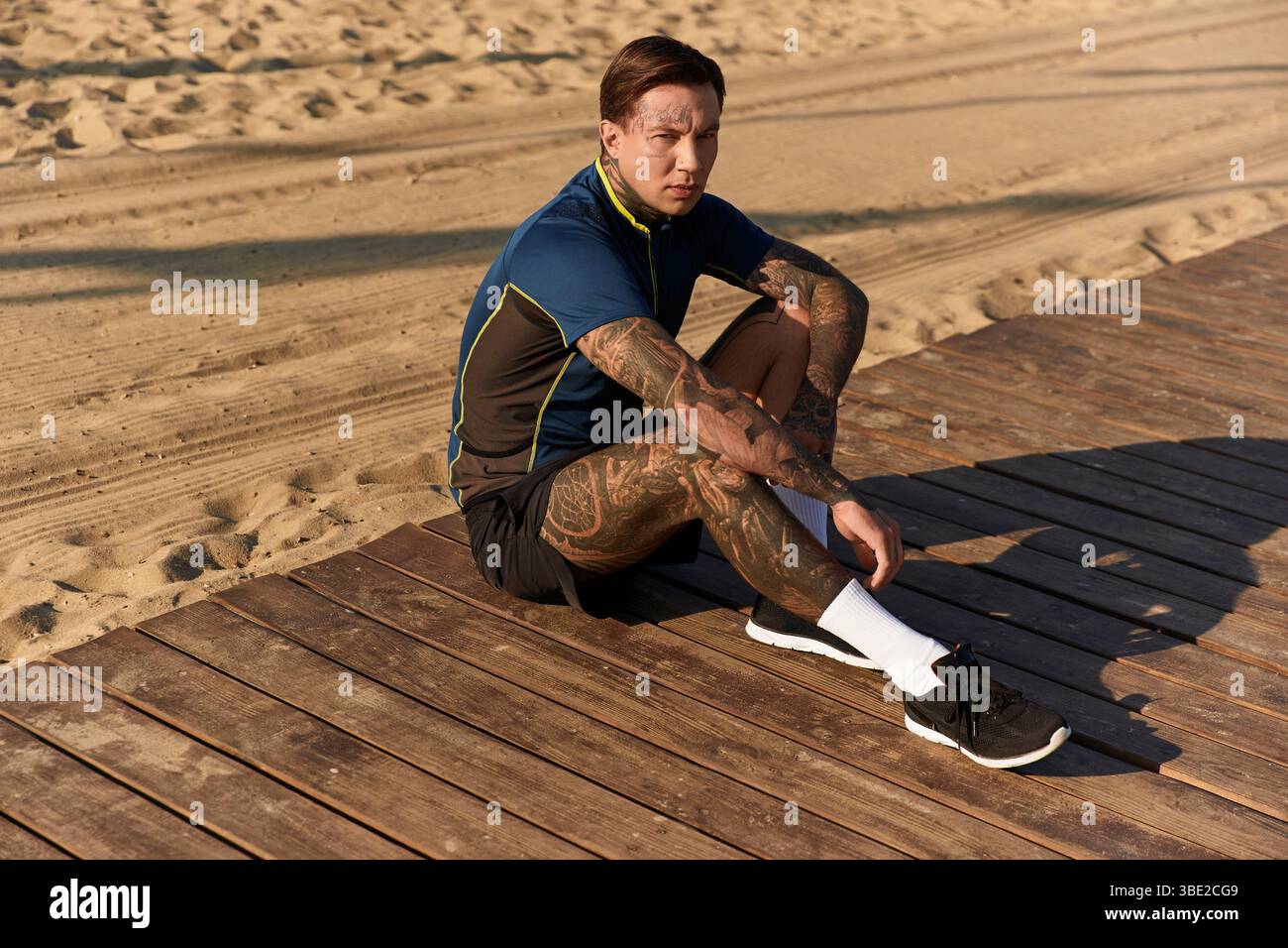 Un jeune homme beau repose sur des planches de bois, profitant d'une promenade ensoleillée au bord de l'eau. Banque D'Images