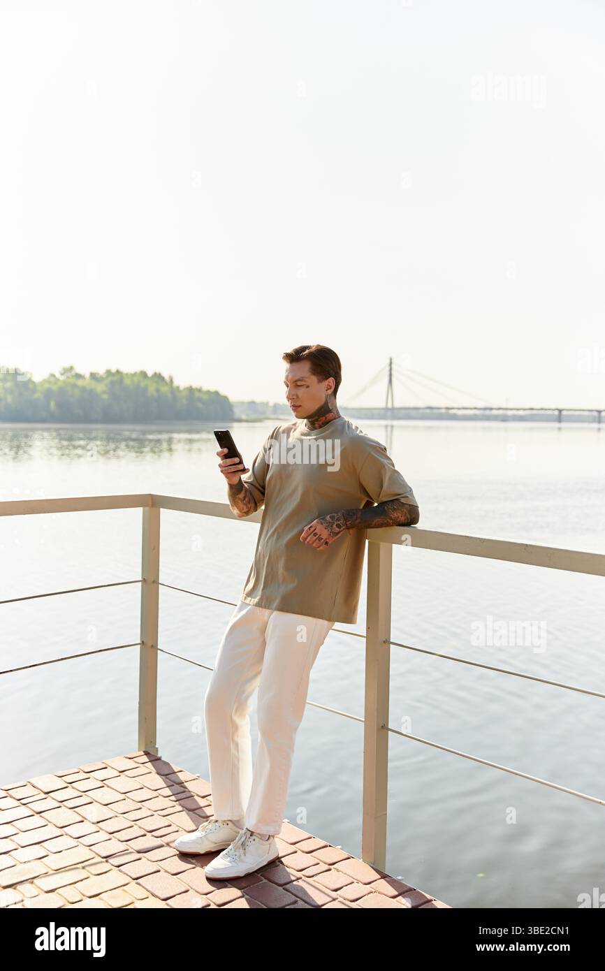 Beau jeune homme se penche contre une balustrade au bord de l'eau, profitant d'une journée ensoleillée sur sa promenade. Banque D'Images