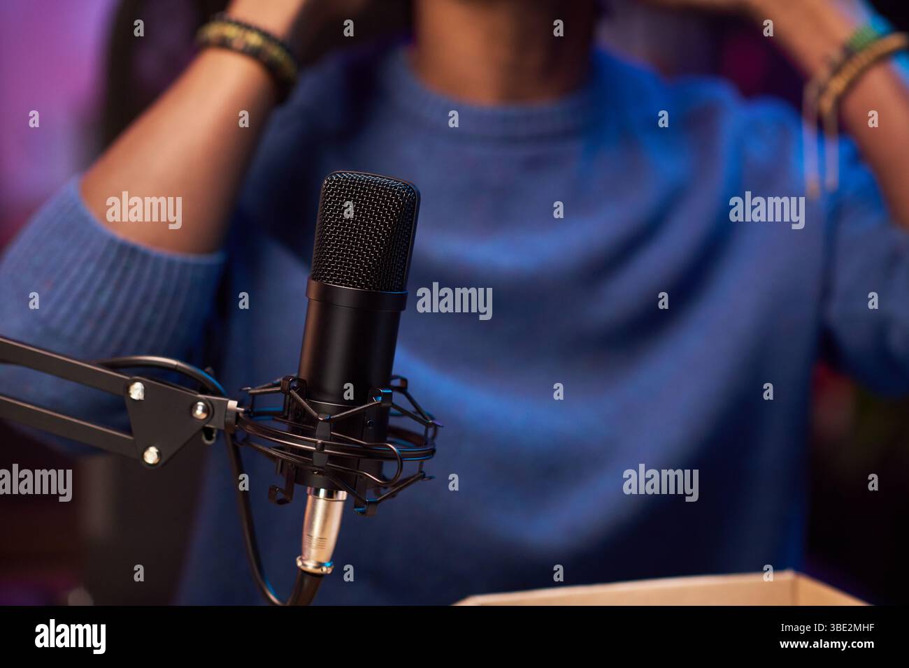 Microphone professionnel placé sur une installation de podcast capturant un son clair avec une personne faisant des gestes en arrière-plan vêtue d'une tenue bleue pour créer un contenu attrayant Banque D'Images