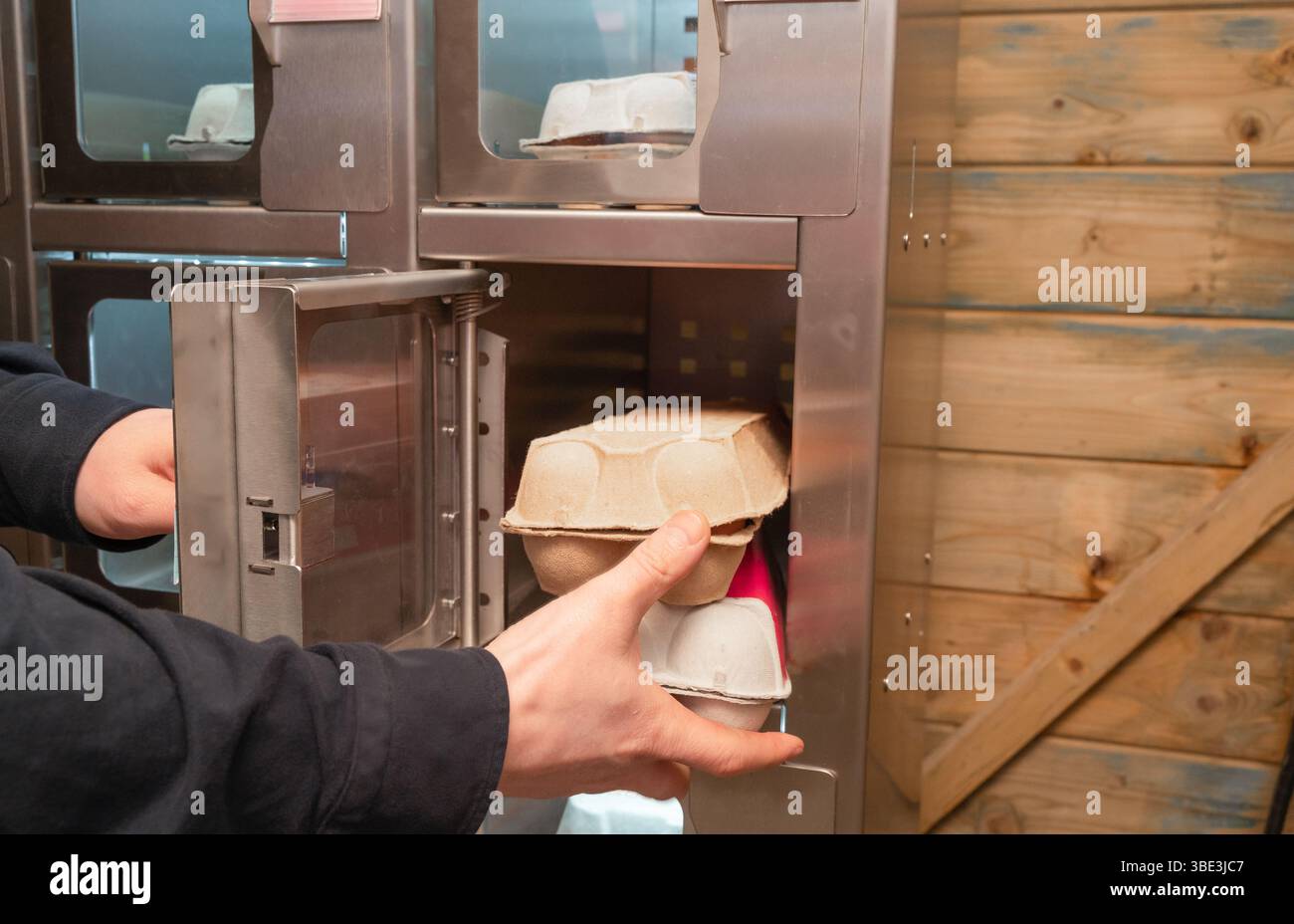 Une personne se tient debout avec un carton d'oeufs tenu devant un distributeur automatique, se préparant à choisir un article de celui-ci Banque D'Images
