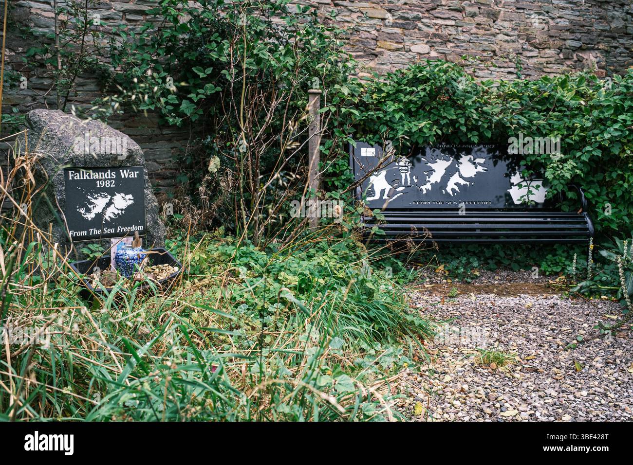 Un banc et un socle commémorant ceux qui sont morts dans la guerre des Malouines dans le jardin de la paix, Brecon, pays de Galles, Royaume-Uni. Le banc est envahi par la végétation. Banque D'Images
