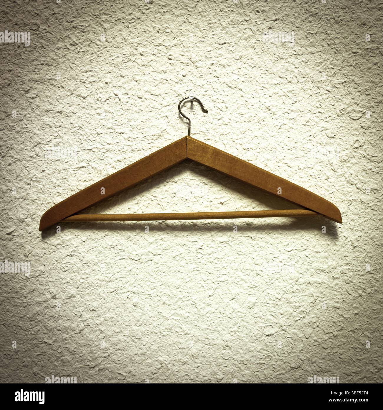 Un cintre en bois repose sur un mur texturé, mettant en valeur sa finition et son design naturels. La scène met l'accent sur le minimalisme, mettant en évidence la pratique Banque D'Images