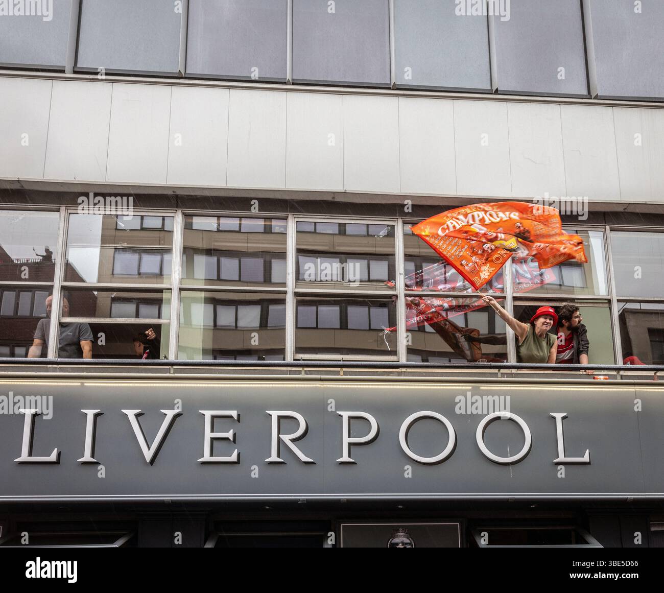 Le supporter de Liverpool agitant le drapeau de la fenêtre célébrant lors de la parade de la victoire du Liverpool FC premier League à Liverpool, le 26 mai 2025 Banque D'Images