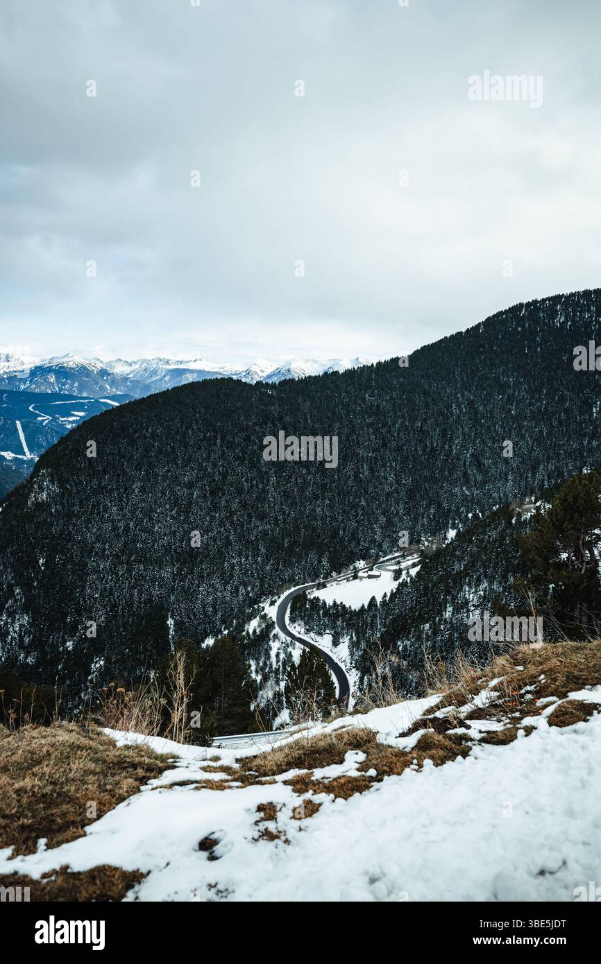 Une route sinueuse serpente à travers un paysage de montagne enneigé en Andorre. Le ciel couvert ajoute une tonalité fraîche, améliorant la vue spectaculaire de la couverture à feuilles persistantes Banque D'Images