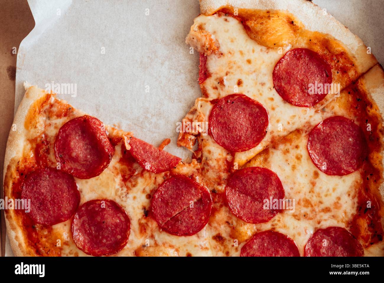 Vue d'en haut, un gros plan d'une pizza pepperoni partiellement mangée avec du fromage fondu et des bords croustillants, reposant sur du papier sulfurisé. Banque D'Images