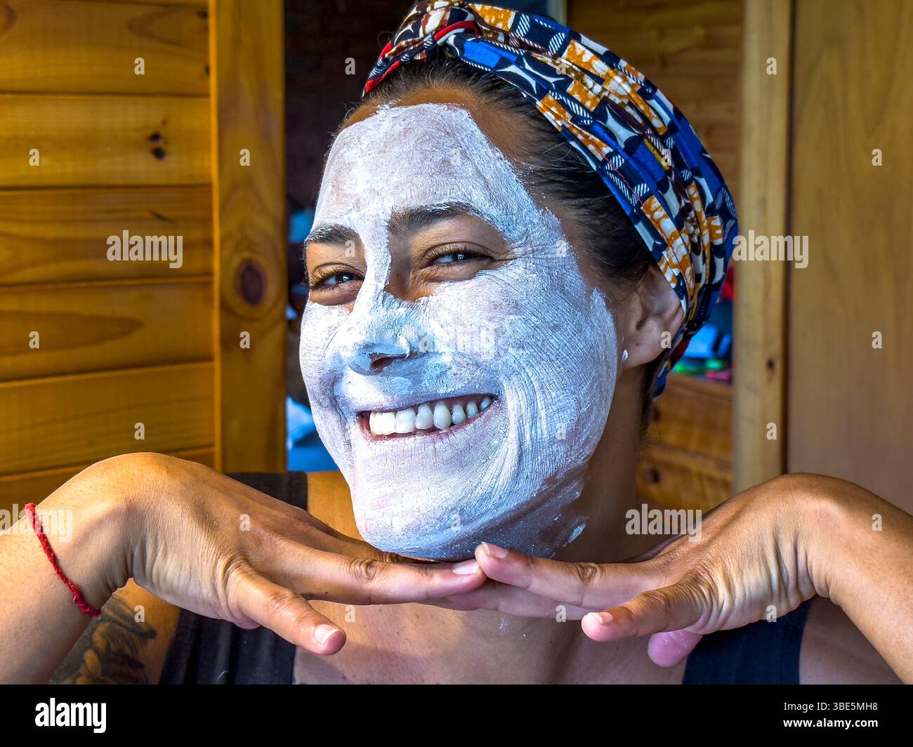 Une femme souriante avec un masque blanc appliqué, posant de manière ludique dans une cabine en bois confortable à Victoria, en Australie. Sa tête est enveloppée d'une cicatrice colorée Banque D'Images