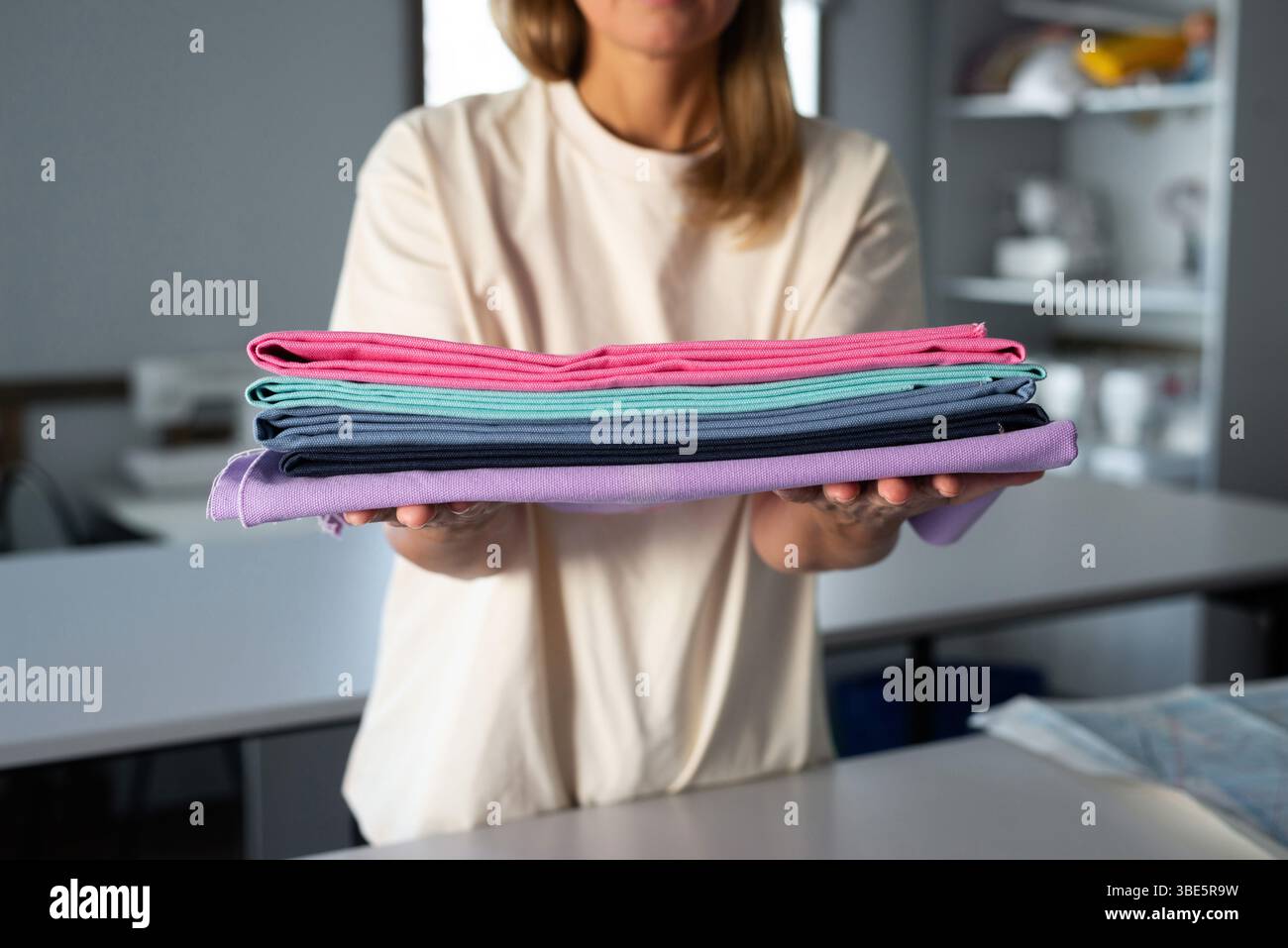 Une femme dans un atelier de couture tient des tissus colorés soigneusement pliés. L'image capture l'essence de la créativité et de l'artisanat, avec des tissus en vib Banque D'Images