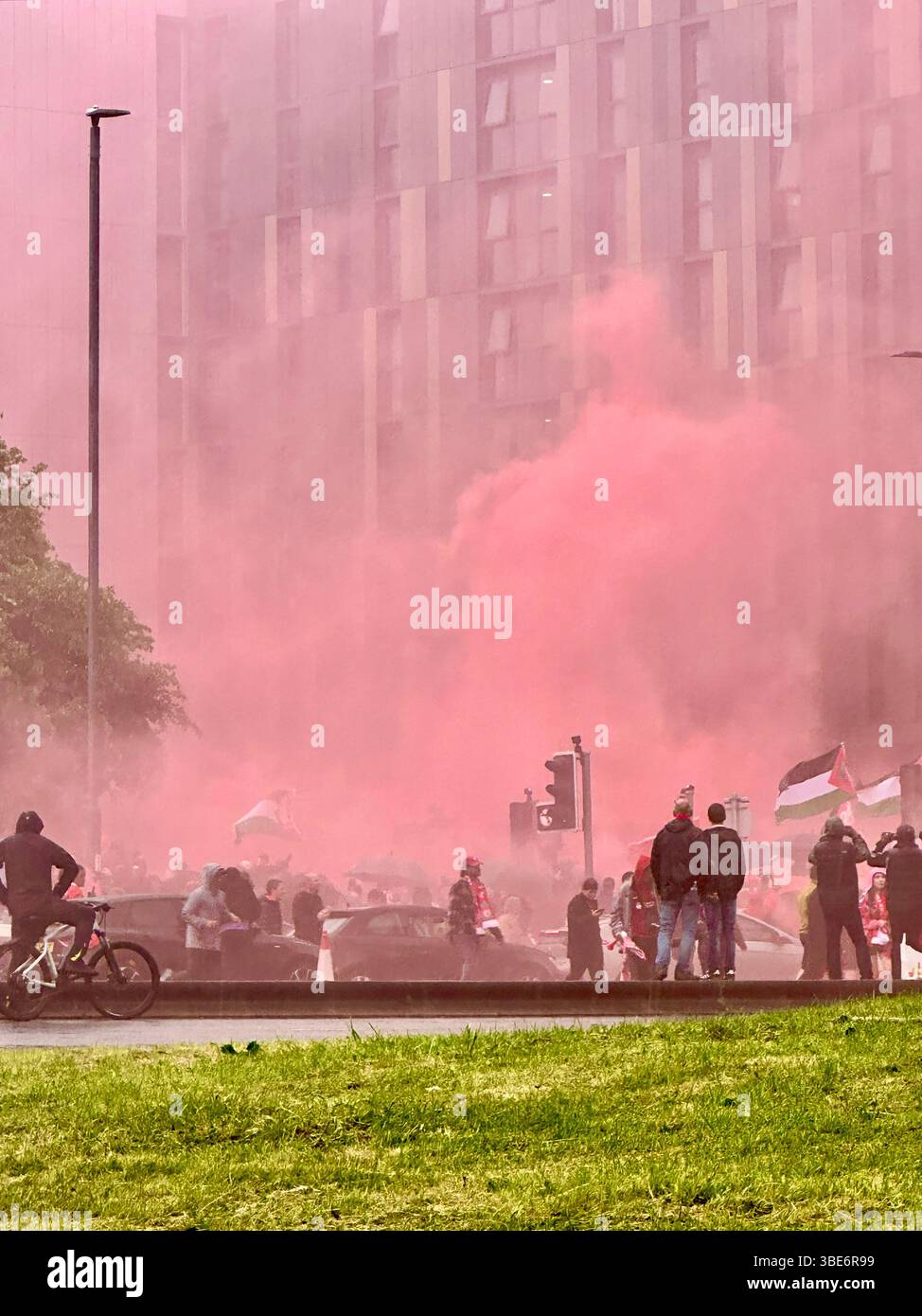 De la fumée rouge envahit Hunter Street, Liverpool, Royaume-Uni, tandis que les fans regardent en haut en attendant le bus de la victoire de la premier League. 26 mai 2025. - Image de stock capturée avec un smartphone