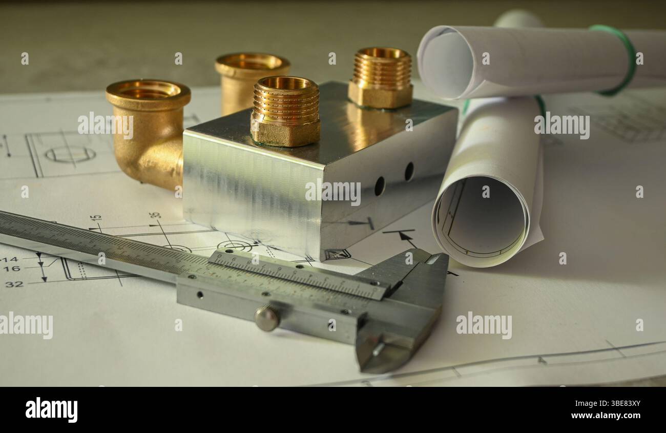 Projet de plomberie montrant les raccords de tuyauterie en laiton, l'étrier et les plans roulés sur le dessus d'un dessin technique. Banque D'Images
