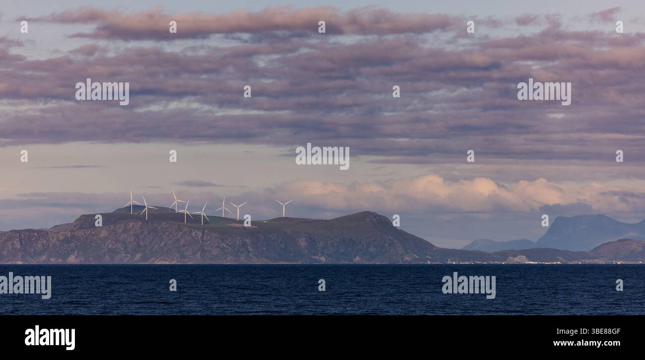 Une rangée d'éoliennes sur les collines côtières norvégiennes vues de l'autre côté de l'océan au crépuscule, avec des cieux pastels et des nuages en couches. Banque D'Images Une rangée d'éoliennes sur les collines côtières norvégiennes vues de l'autre côté de l'océan au crépuscule, avec des cieux pastels et des nuages en couches. Banque D'Images