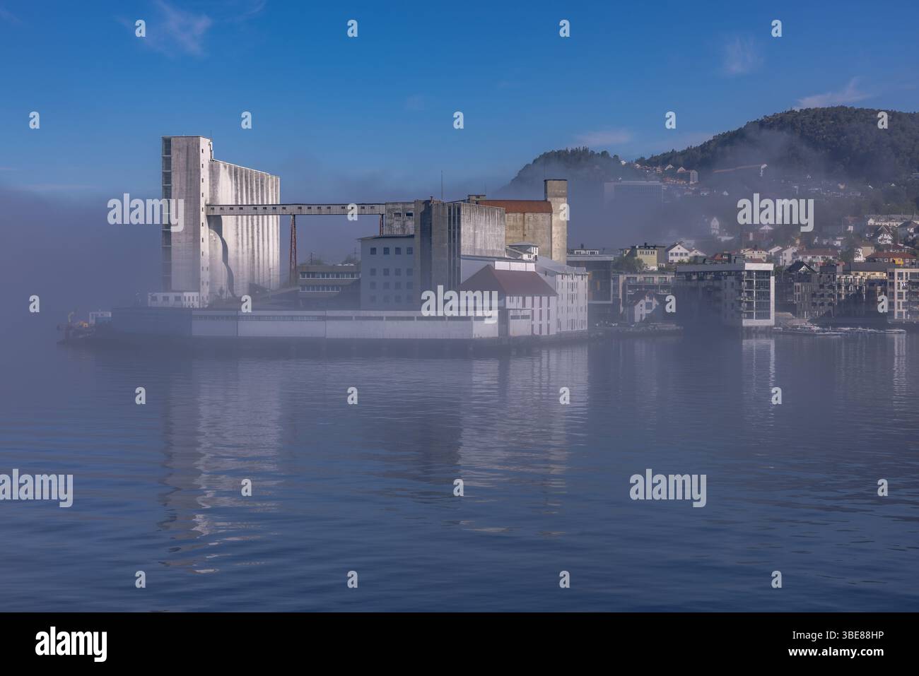 Terminal céréalier industriel et bâtiments riverains partiellement obscurcis par la brume matinale à Bergen, Norvège. Banque D'Images