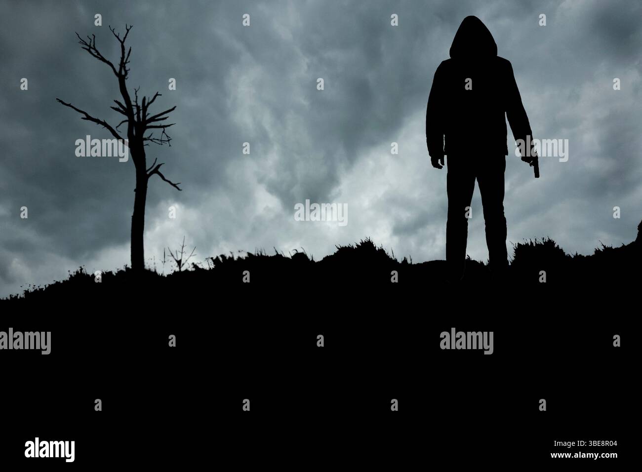 silhouette d'un homme avec une arme à feu par un arbre mort Banque D'Images