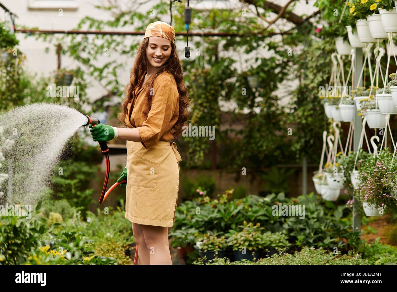 Charmante jardinière féminine avec un foulard tendant aux plantes dans une serre ensoleillée. Banque D'Images