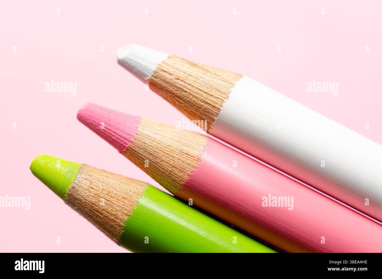 Gros plan de trois crayons de couleur dans des couleurs pastel sur fond rose. Banque D'Images