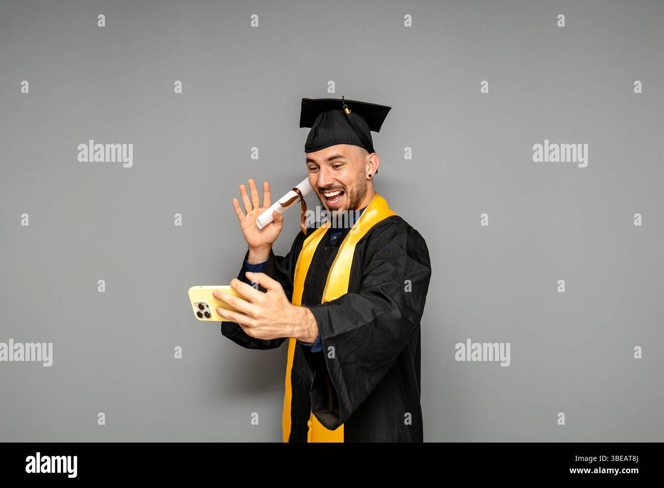 Heureux diplômé faisant appel vidéo montrant le diplôme tout en portant la robe et la casquette Banque D'Images