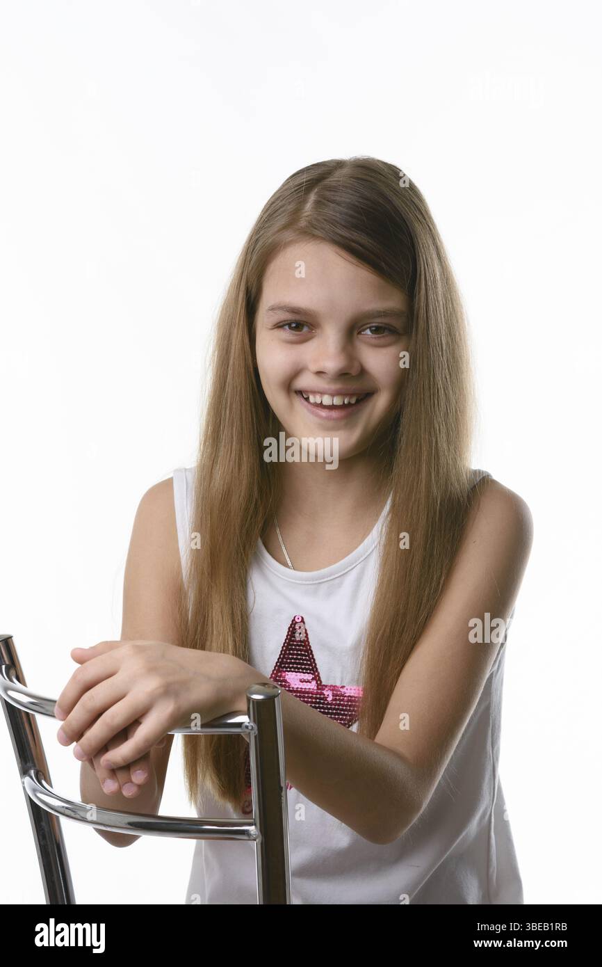 Fille assise sur une chaise à haut dossier et souriante joyeusement Banque D'Images