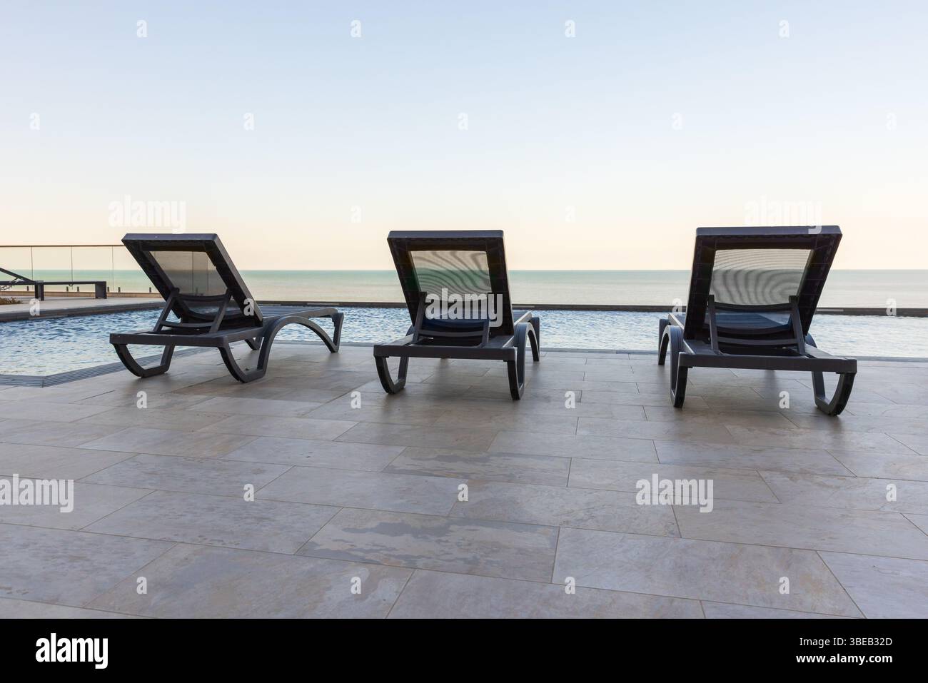 Découvrez la tranquillité avec une vue panoramique sur un océan calme et des chaises longues modernes près d'une piscine immaculée à débordement, parfait pour la détente ou un petit bol serein Banque D'Images