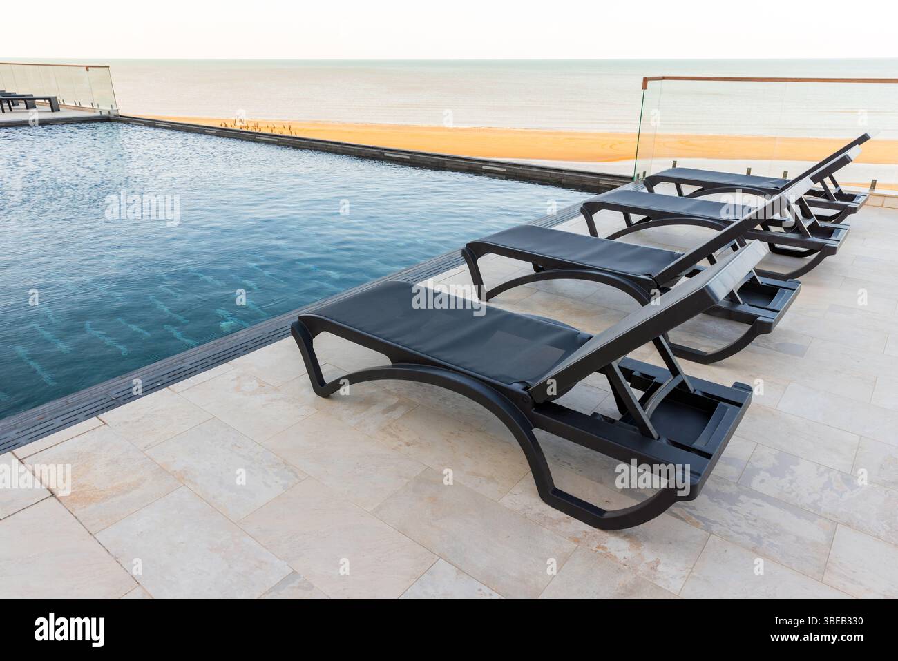 Une piscine à débordement accueillante avec chaises longues inclinables en bord de mer, offrant tranquillité et luxe Banque D'Images