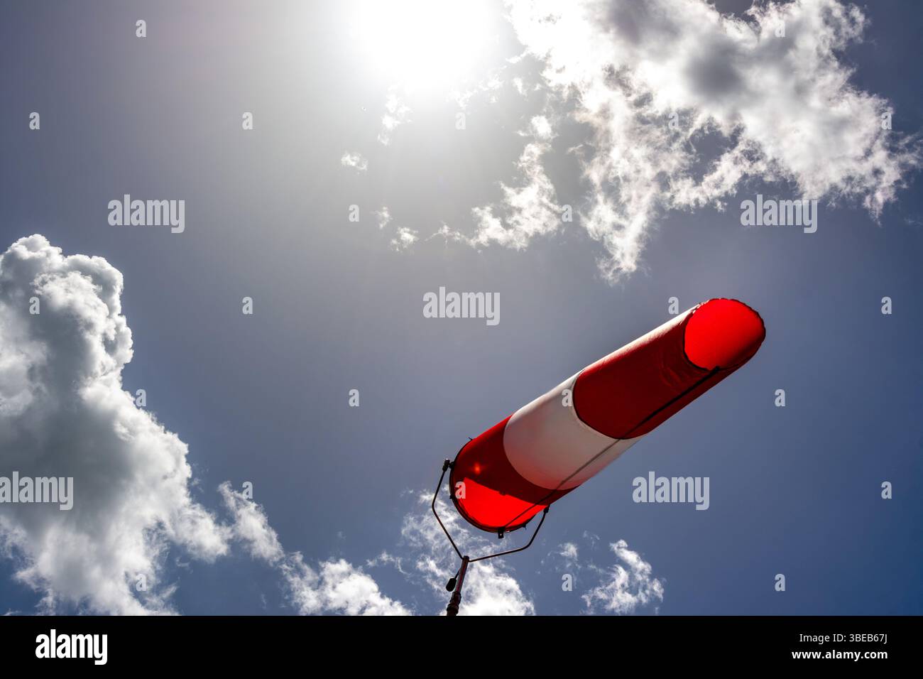 Une chaussette colorée est suspendue à un haut poteau, indiquant clairement la direction du vent. Le ciel lumineux est rempli de nuages dispersés, créant un arrière-plan vif Banque D'Images