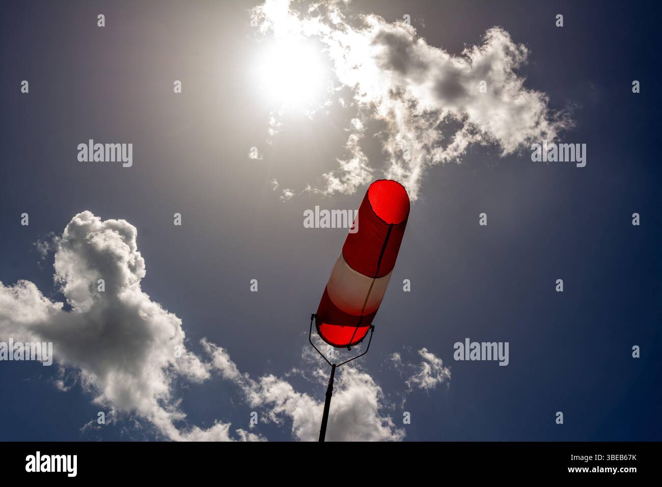 Une chaussette colorée est suspendue à un haut poteau, indiquant clairement la direction du vent. Le ciel lumineux est rempli de nuages dispersés, créant un arrière-plan vif Banque D'Images