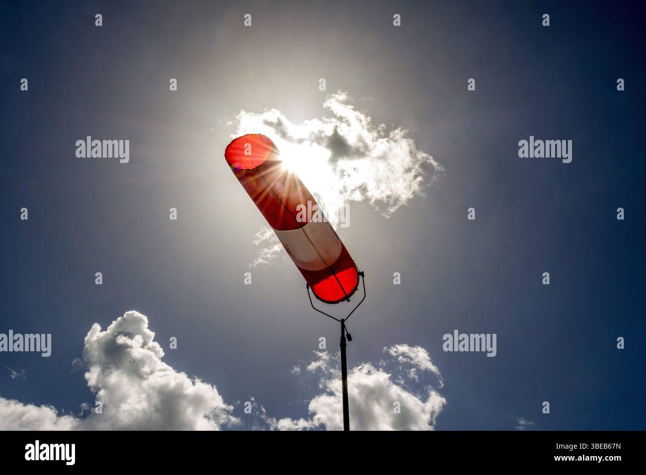 Une chaussette colorée est suspendue à un haut poteau, indiquant clairement la direction du vent. Le ciel lumineux est rempli de nuages dispersés, créant un arrière-plan vif Banque D'Images