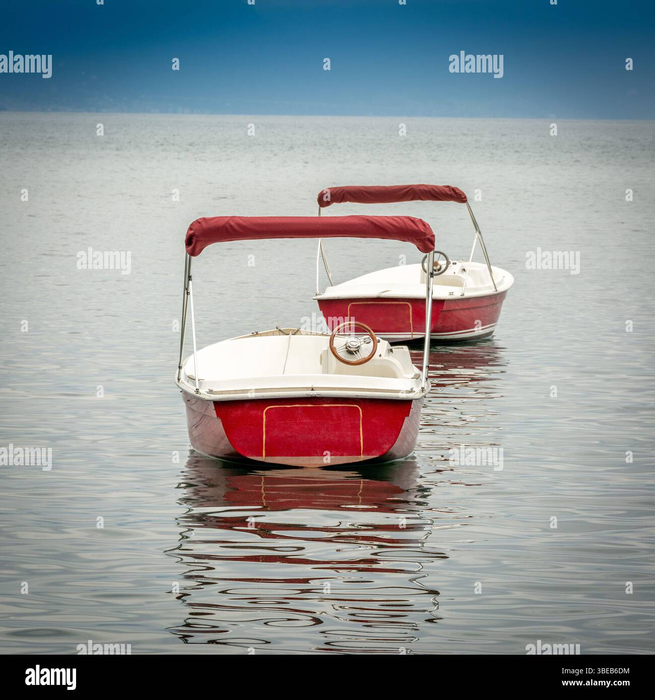 Plusieurs petits bateaux rouges reposent sur la surface paisible du lac Léman, reflétant le ciel bleu clair. Suisse Banque D'Images